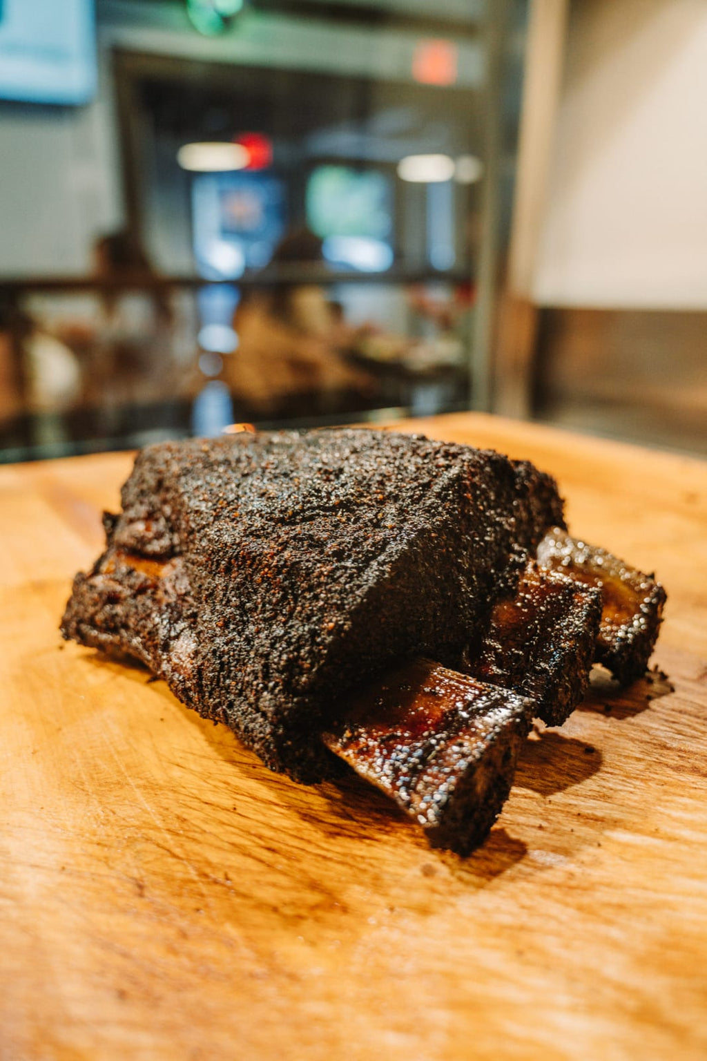 A smoked dino beef rib with a dark peppery bark on the cutting board