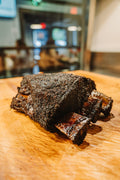 A smoked dino beef rib with a dark peppery bark on the cutting board