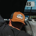 Hexagon Patch Trucker Hat in tan with a black mesh back, worn at the smoker